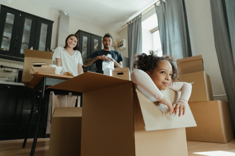 Couple unpack boxes as daughter sits in a box