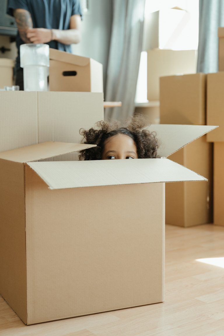 Daughter peering out of cardboard box with dad behind