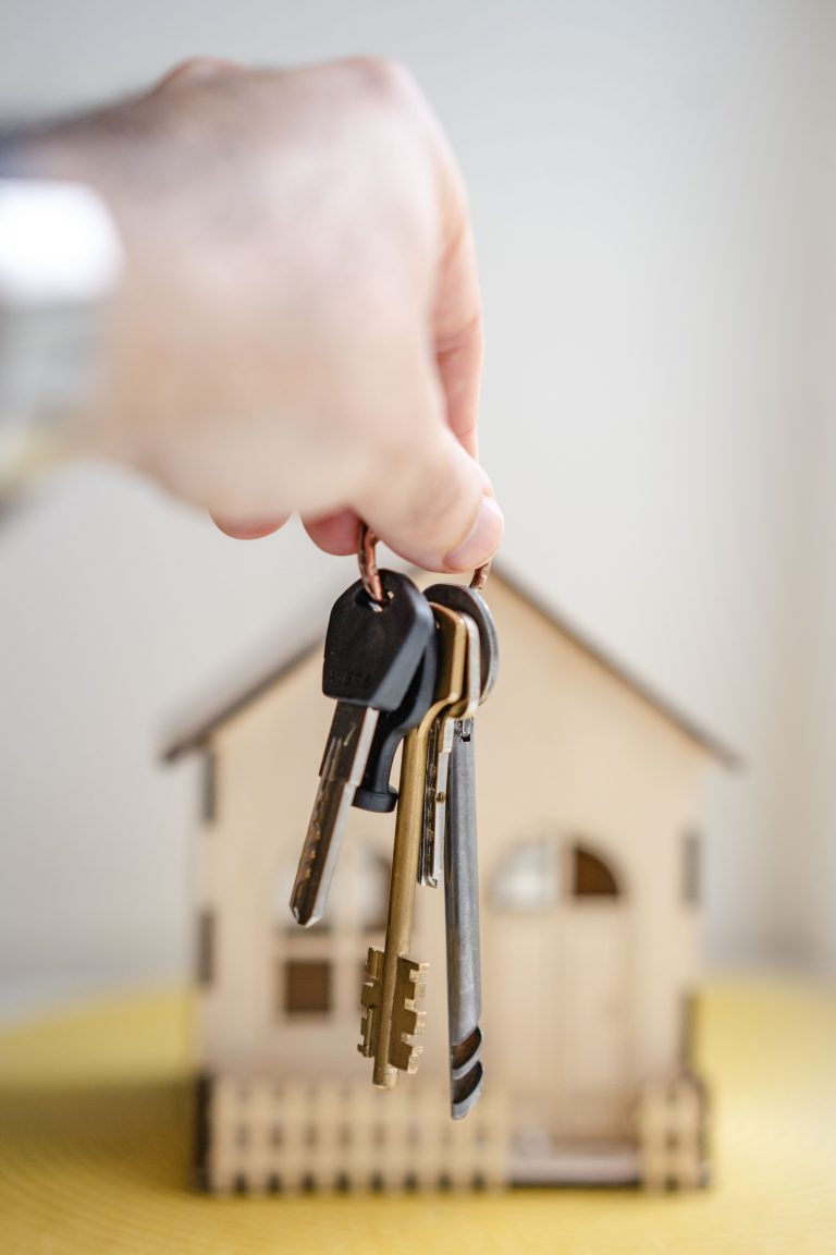 Hand dangles keys in front of small model home