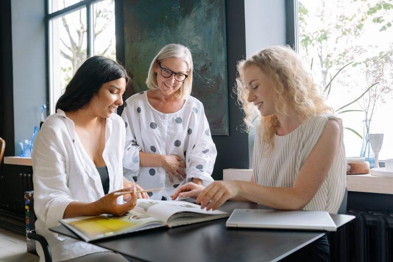 Three women flipping through book smiling