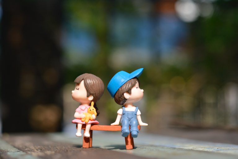 Tiny toy boy and girl sit together looking away from each other