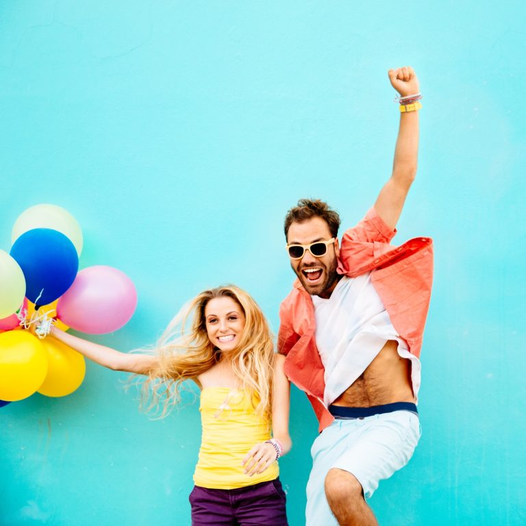 Excited couple holding balloons jump with arms raised