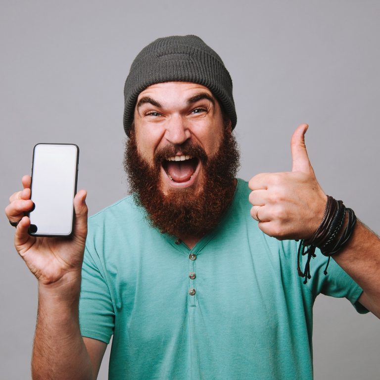 Excited bearded man holds phone and gives thumbs up