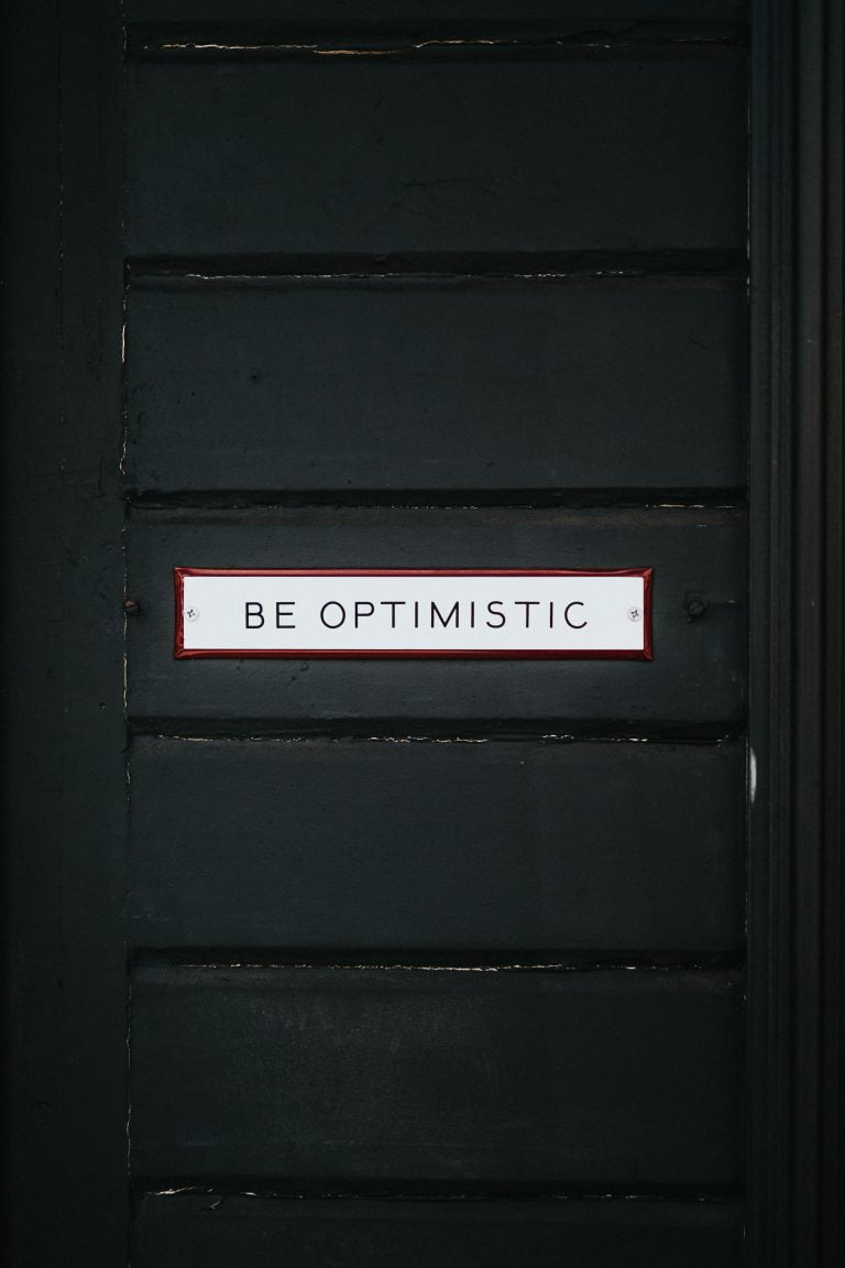 Black door with sign reading be optimistic