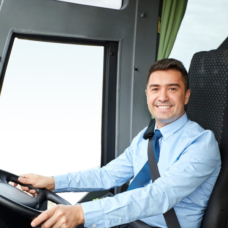 Bus driver in a blue shirt and tie smiles behind the wheel