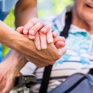 Care giver clasps hand of elderly lady in a wheel chair