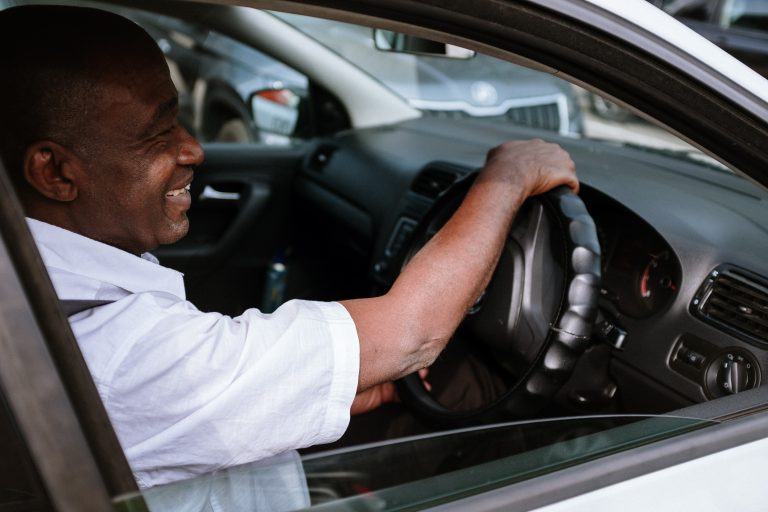 Elderly male driver smiles with one hand on the steering wheel