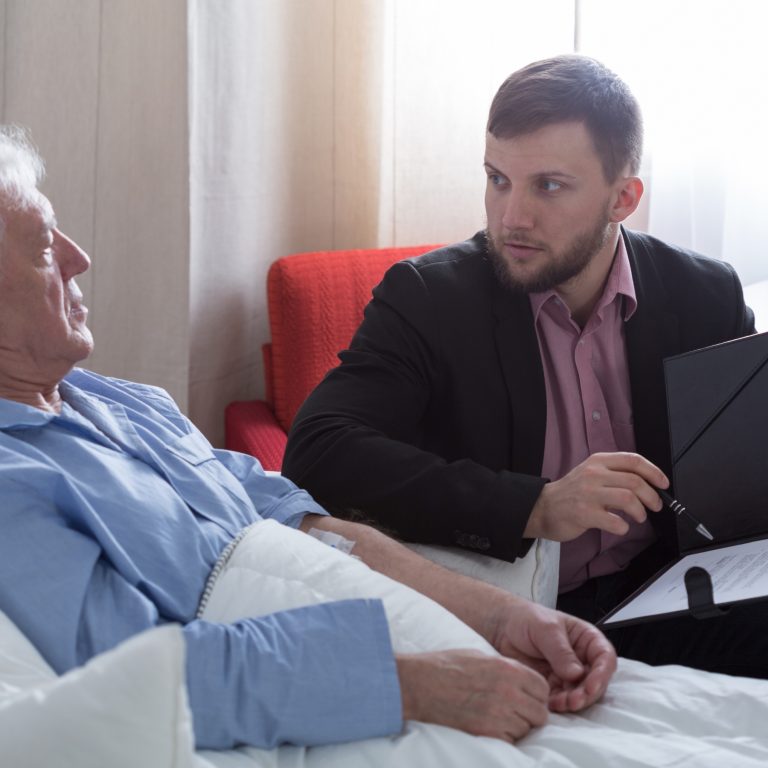 Elderly man in bed reviewing power of attorney with lawyer