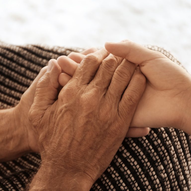 Elderly person holds younger persons hand in his hands