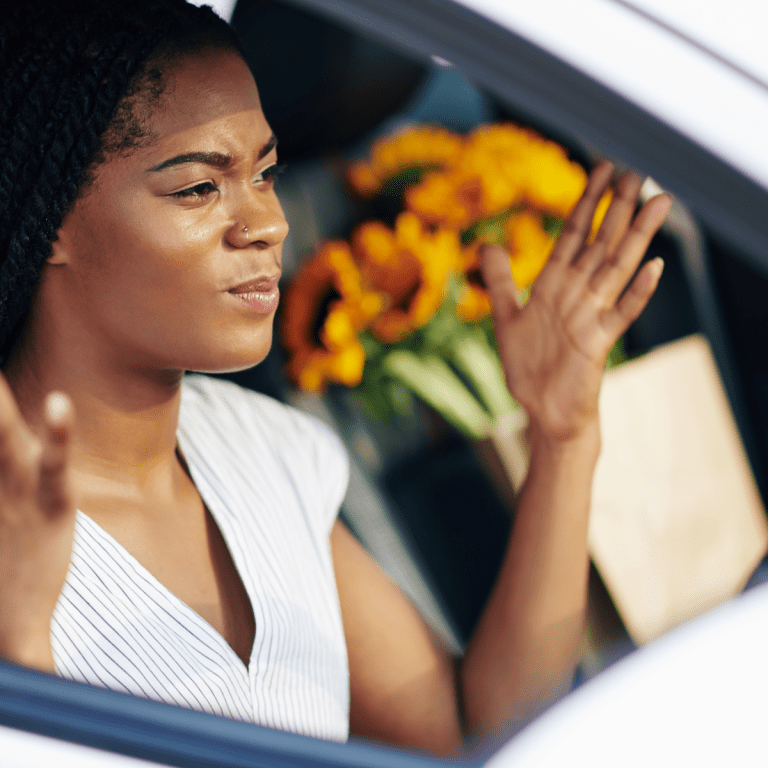 Female driver confused throws hands in the air while in drivers seat