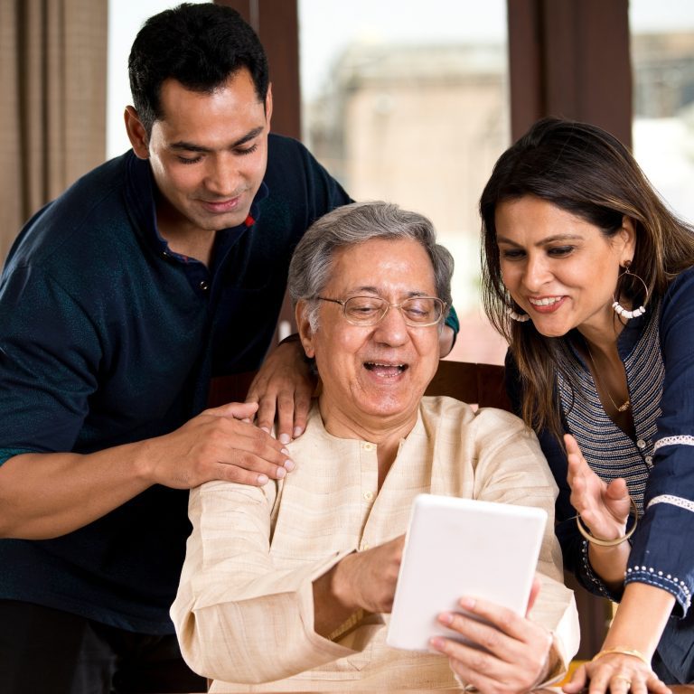 Granddad holds tablet and laughs as son and daughter lean in on his screen