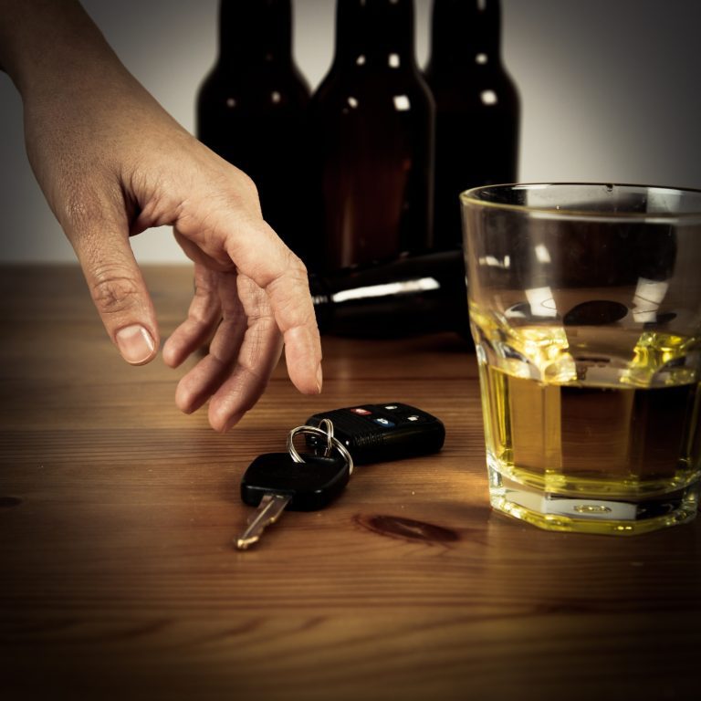 Hand reaches for car keys on a table next to alcohol