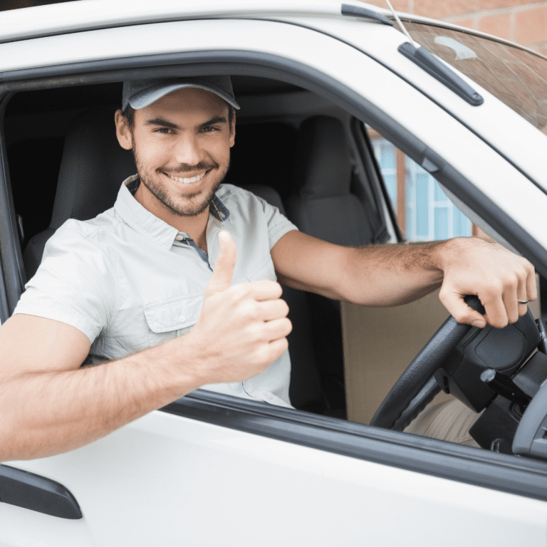 Male driver smiles with one hand on steering wheel the other gives thumbs-up