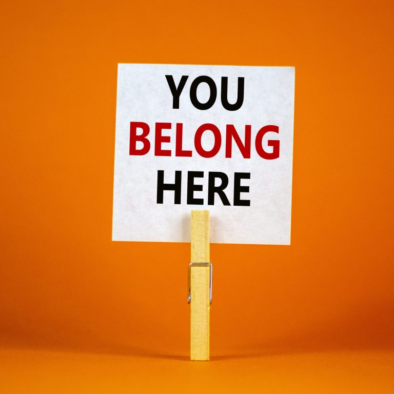 Paper with you belong here held by peg on orange background