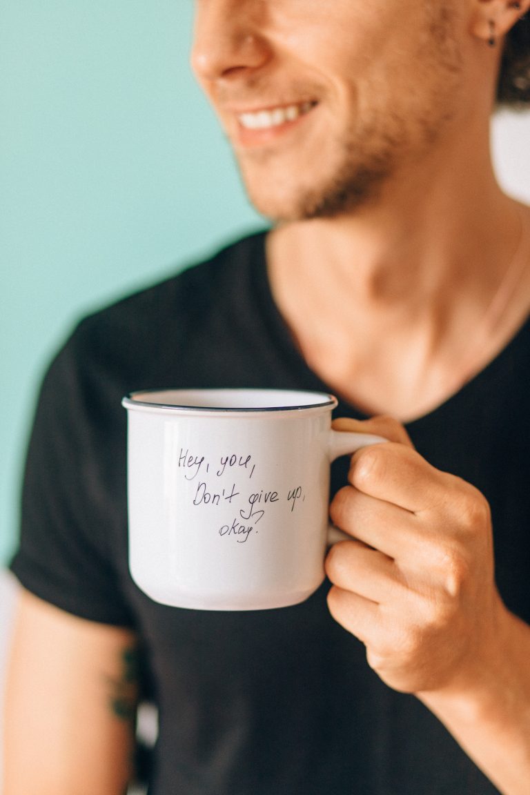 Smiling man holds cup that reads hey you dont give up okay