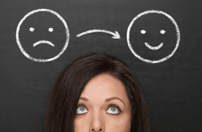 Woman looks up at a sad face emoji with arrow pointing to a happy face emoji