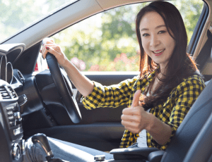 Woman sits in drivers seat and gives thumbs-up smiling