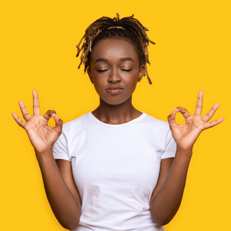 Young lady closes her eyes doing double okay signs against yellow background