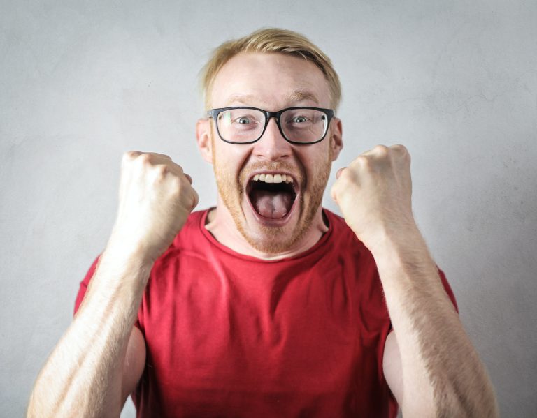 Man wearing glasses and red shirt clenches both fists in excitement