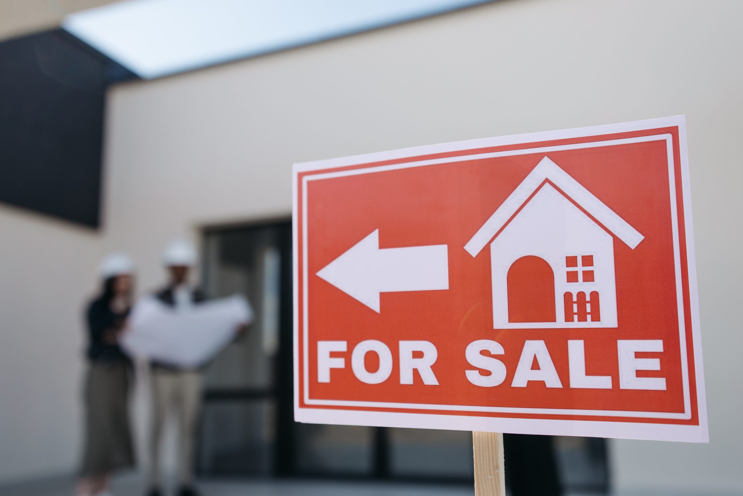 A for-sale sign in front of a house with buyers behind