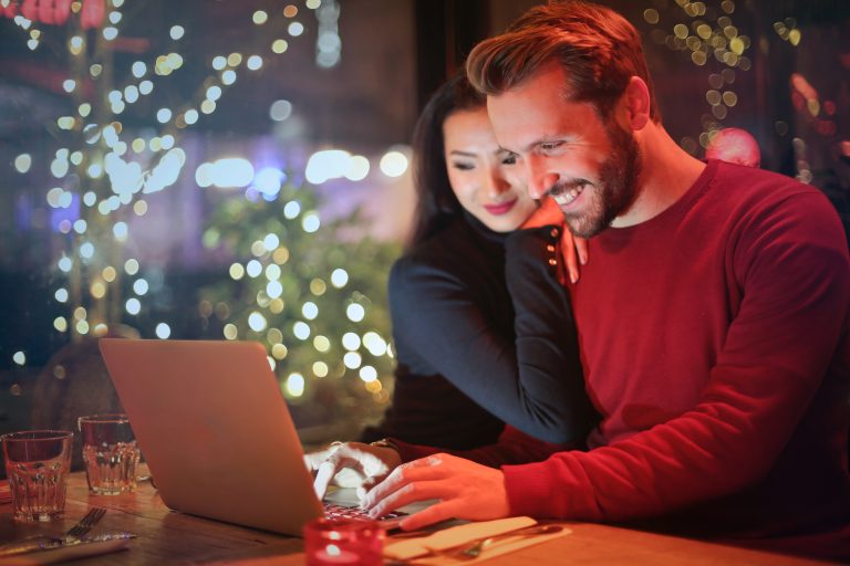 Caucasian couple share smile perusing a laptop at a table