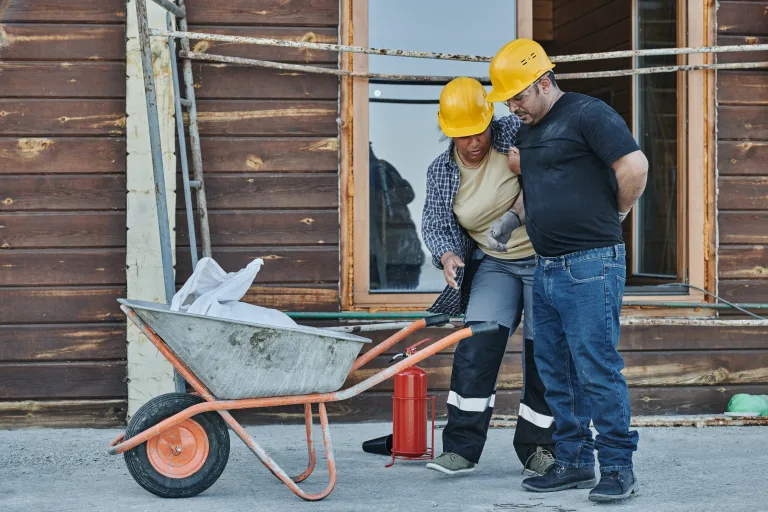 Man hurt in work accident being helped by coworker in hard hats