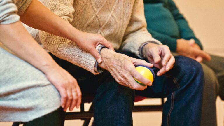Lady holds hand of elderly man holding a ball