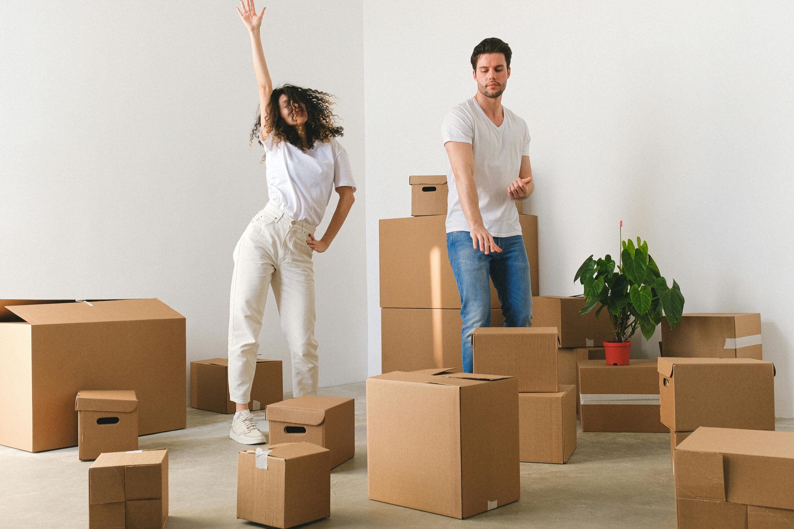 Young couple dance surrounded by moving boxes after getting help for first-time buyers