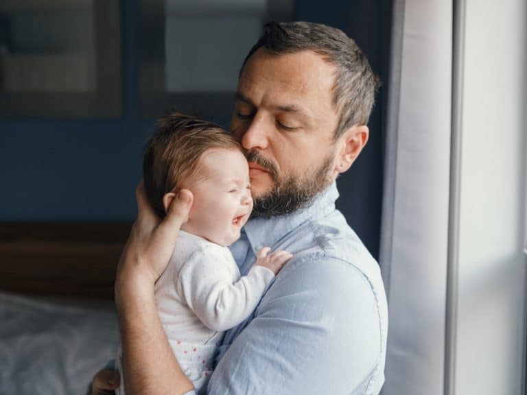 Father tries to soothe his crying baby in his arms, alone in the bedroom, highlighting Scullion LAW's support in divorce, separation, and financial arrangements.