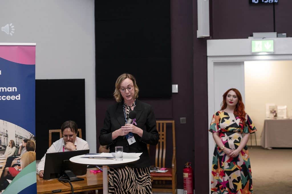 Judith Higson, Head of Family Law at Scullion LAW, standing with a microphone while presenting key awards at the Women’s Business Club Conference 2024.