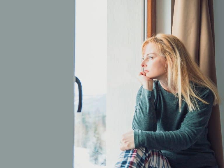 Blonde woman looking out of window, contemplating recent separation.