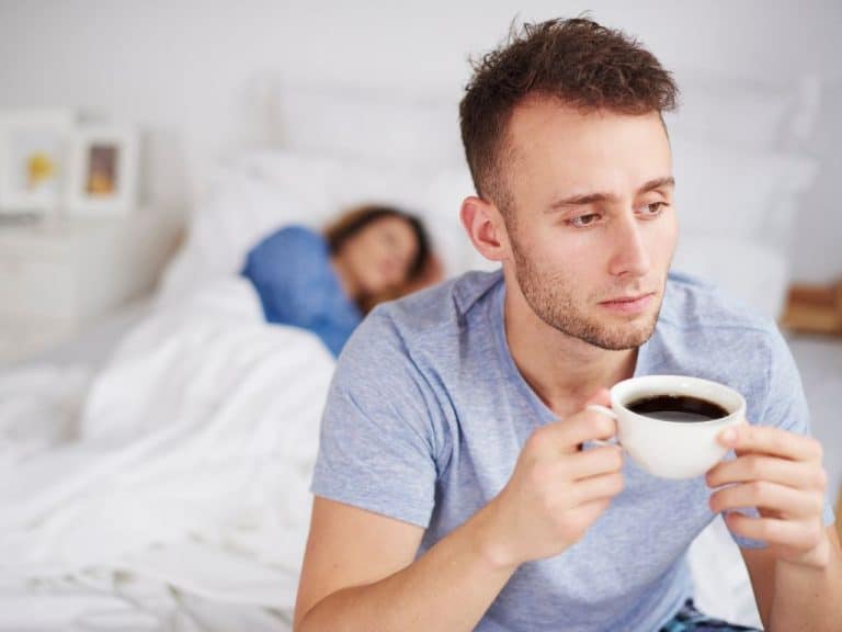 Man sitting up in bed with coffee, contemplating separation from partner