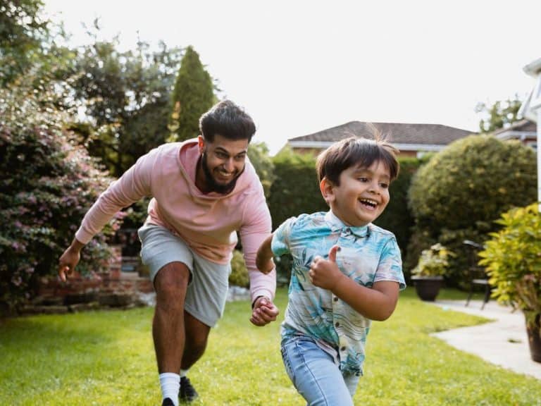 Father chasing his laughing son in the garden, both enjoying a fun moment. The father is contemplating securing his family's future with a Will and Power of Attorney from Scullion LAW.