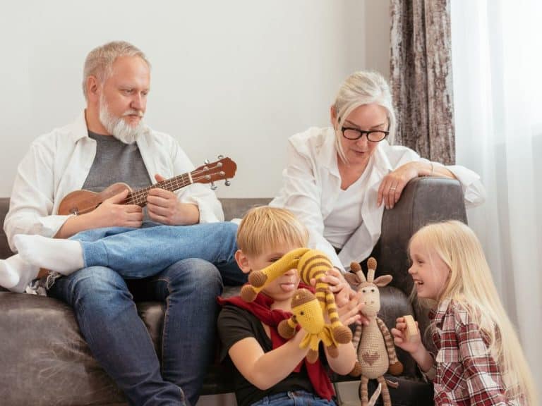 Retired grandparents on sofa with grandchildren at their feet, enjoying time together. They're securing their family's future with a Will and Powers of Attorney.