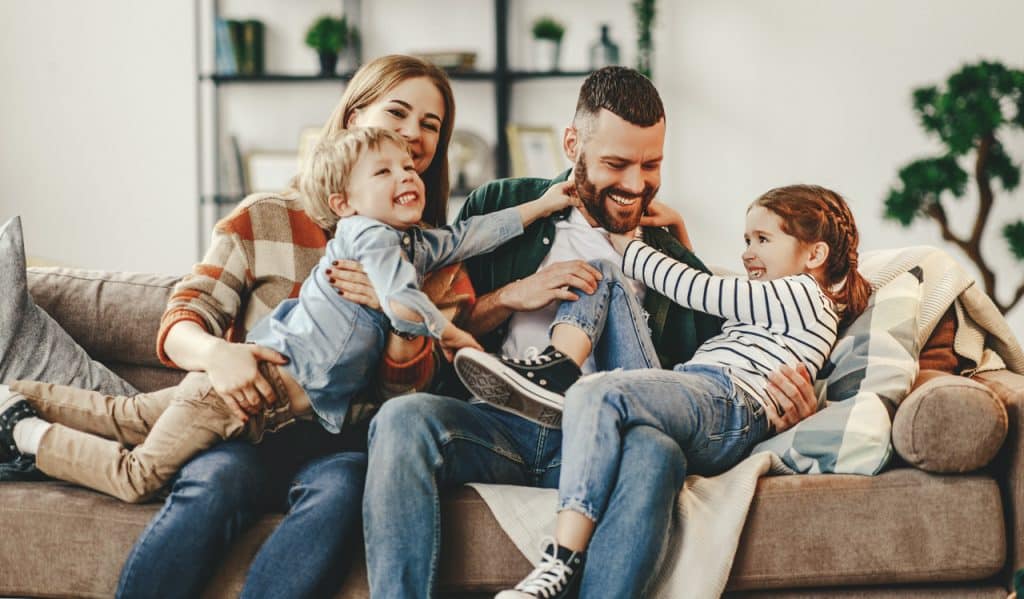 A family of husband, wife and two children playing on a sofa